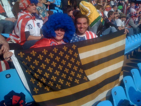 Bywater couple holding a US flag of black and gold with Fleur de Lis instead of stars