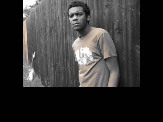 The guitarist Gary Clark Jr. rests on a wooden fence.